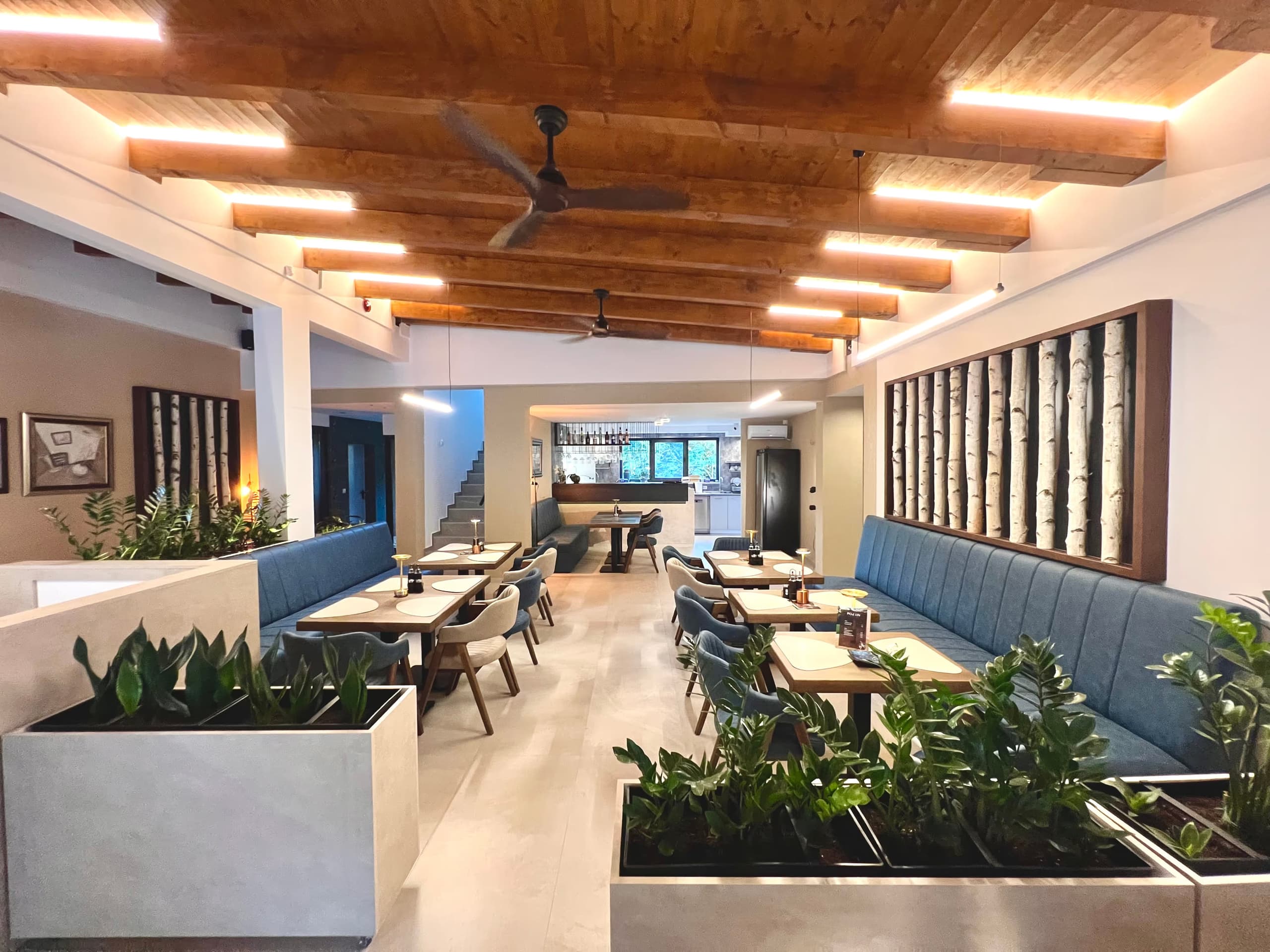Enterijer kafe-restorana sa drvenim plafonom, tirkiznim klupama i zelenilom